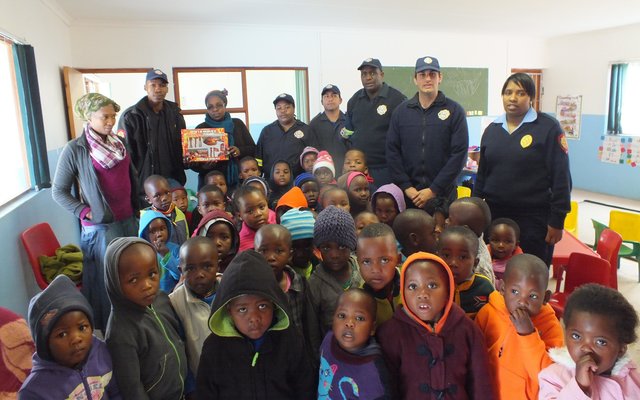 Links agter oorhandig Thembelani Xovula die Brandweerprys van Selina Nqejane (5) van Masakhane Créche aan Gloria Silku, wat dit namens Selina in ontvangs geneem het